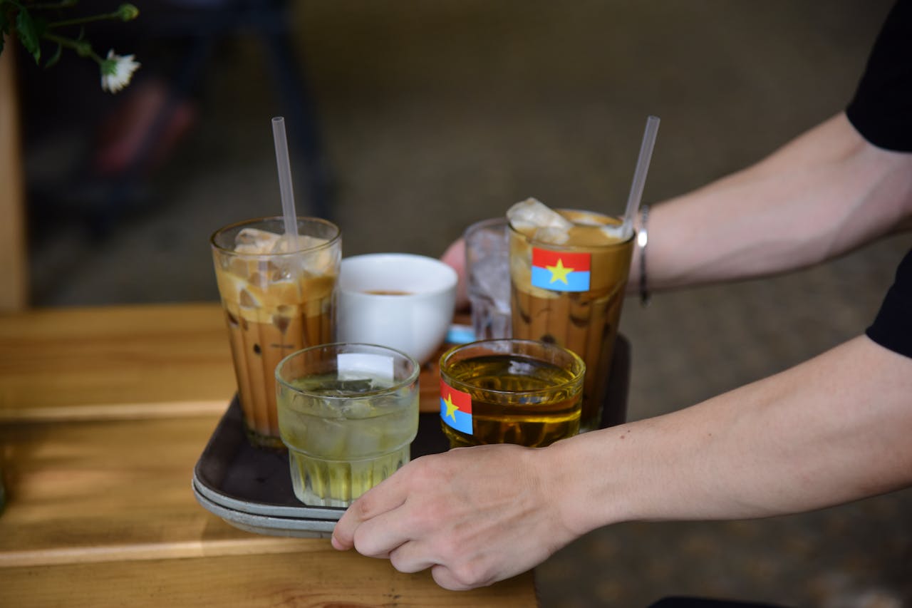 Close-up of a tray with Vietnamese iced coffee, hot cup, and tea on a wooden table.