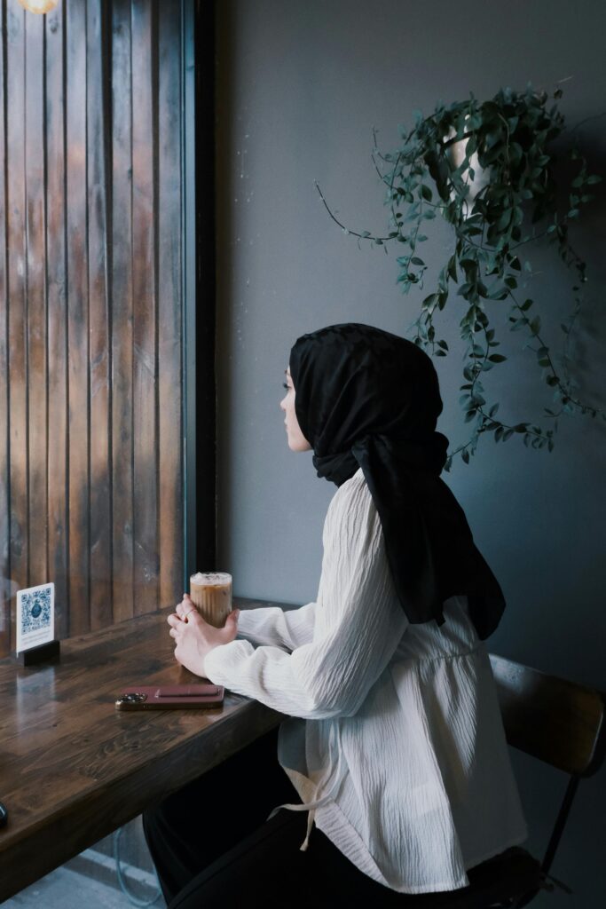 Woman enjoying a cappuccino while gazing out a cafe window, embracing a moment of reflection.