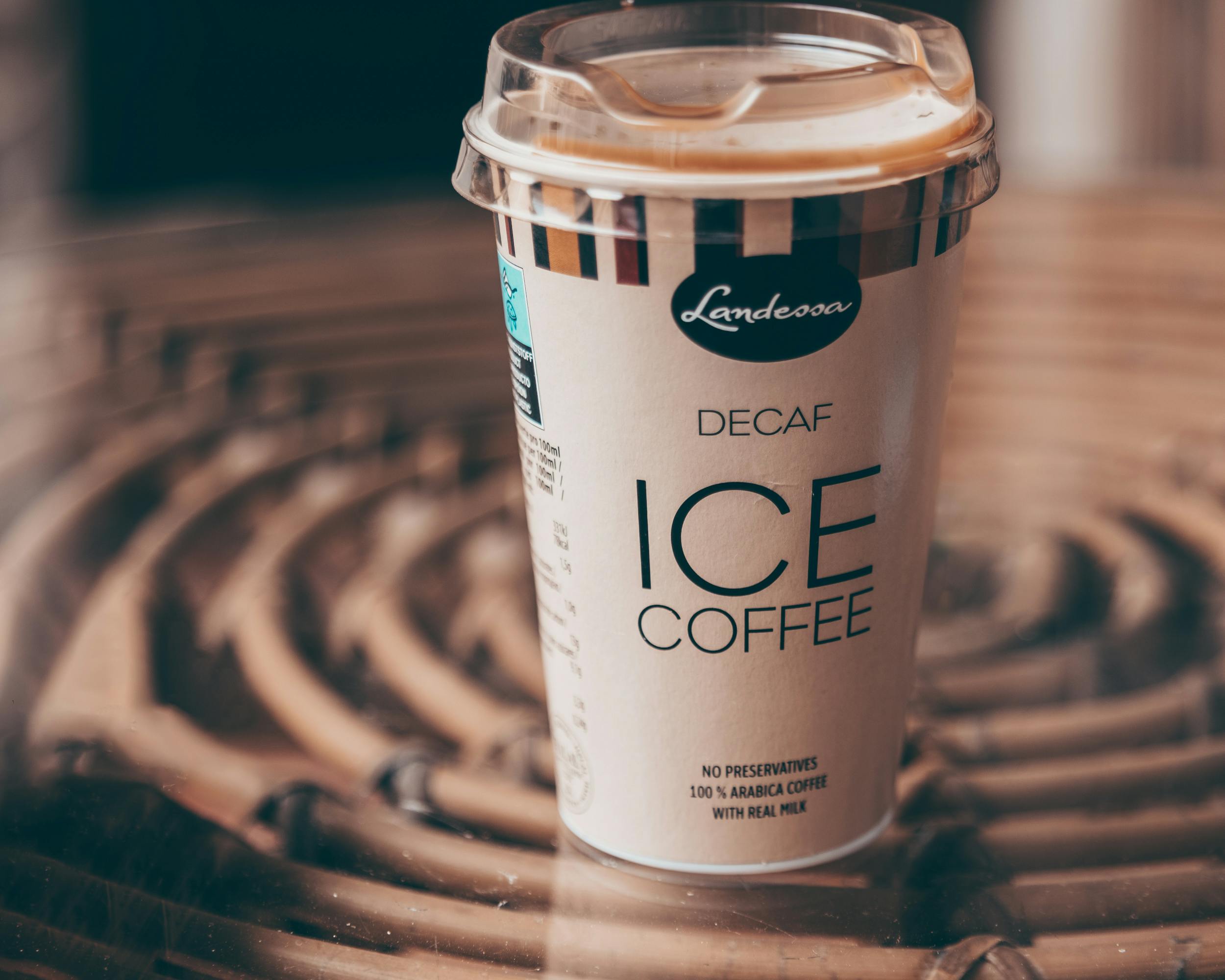 Decaf iced coffee cup with lid on a patterned table, perfect for a refreshing break.