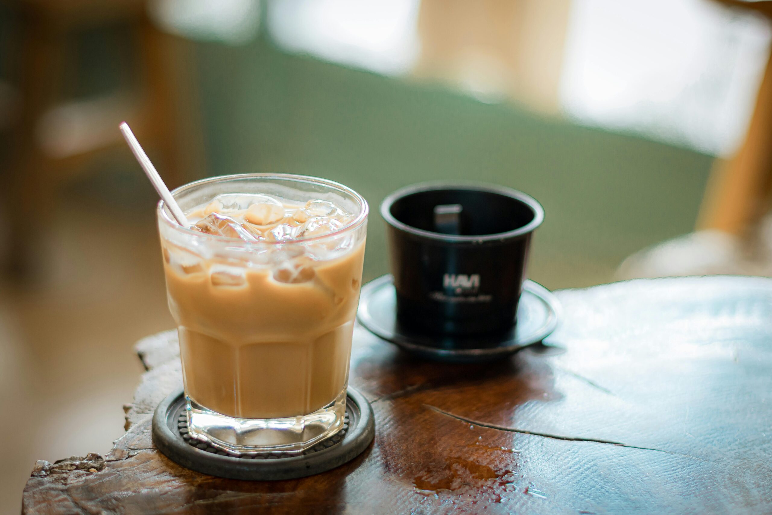 Glass of iced coffee and phin filter on rustic table in cozy cafe setting.