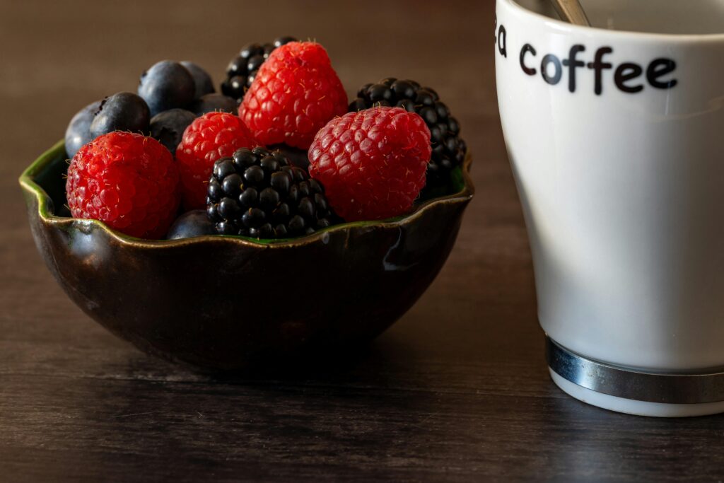 A rustic breakfast scene featuring a bowl of mixed berries and a cup of coffee on a wooden table.