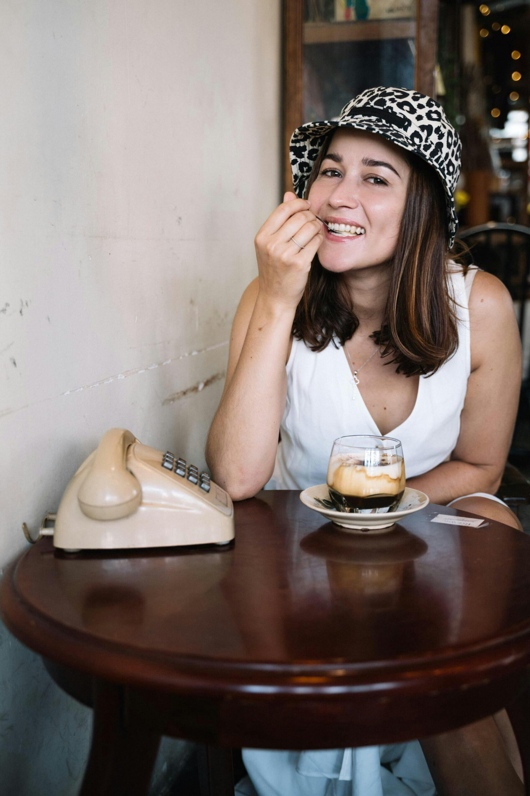 Smiling woman with affogato and retro phone at a cozy cafe.
