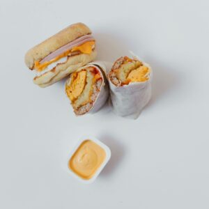 Delicious breakfast burrito and sandwich with cheese dip on a white background, perfect for food photography.