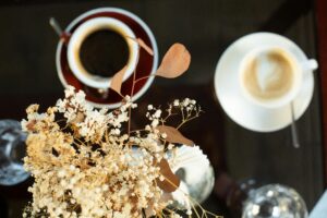 Top view of black and latte coffee with dry floral decor and vase, creating a serene cafe vibe.